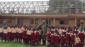 Foto: Pfarrer Charlie mit seinen Schulkindern vor dem Rohbau der neuen Schule, Umulokpa, Nigeria, Juni 2013